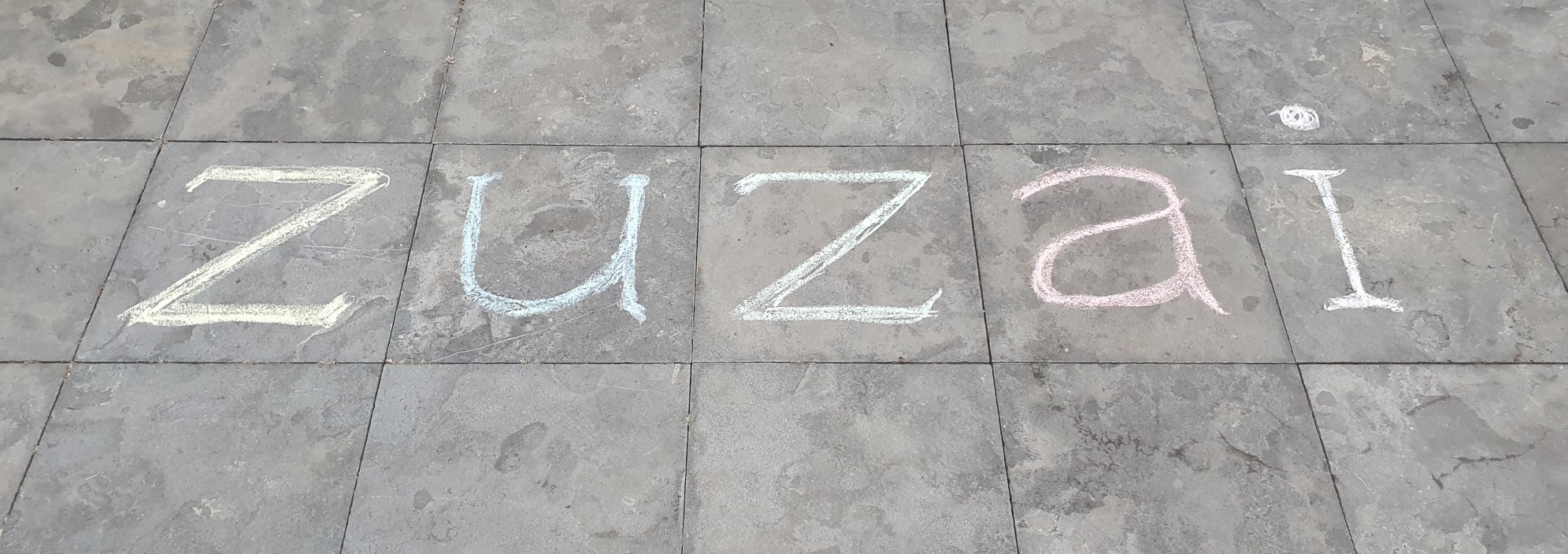 A photo of the word 'zuzai' written in multicolored chalk on flagstones